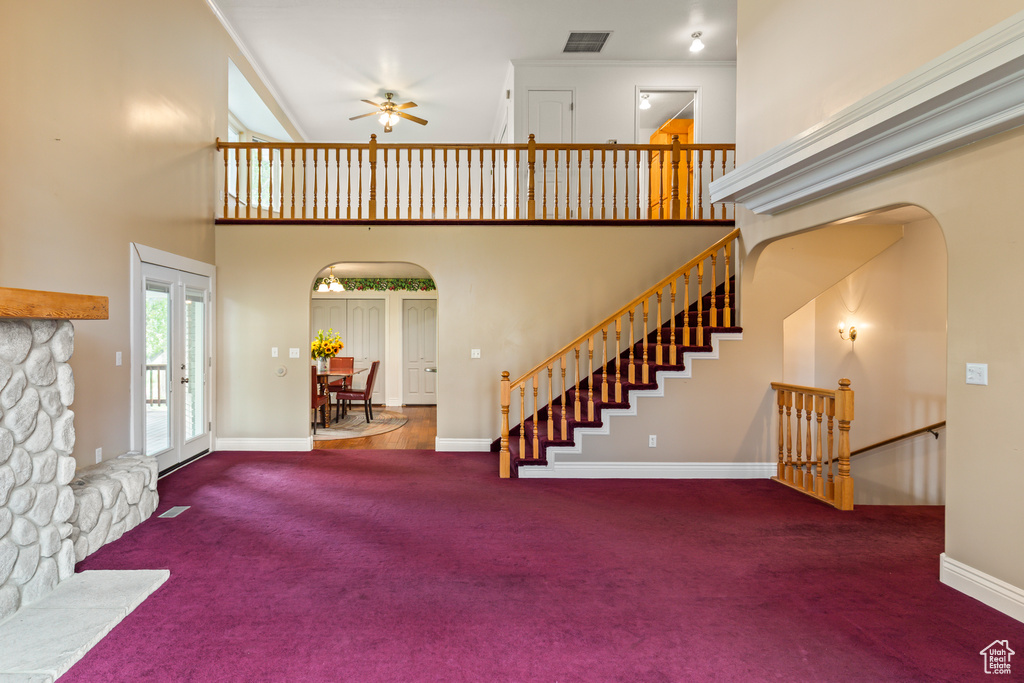 Unfurnished living room featuring carpet, arched walkways, a ceiling fan, a towering ceiling, and baseboards