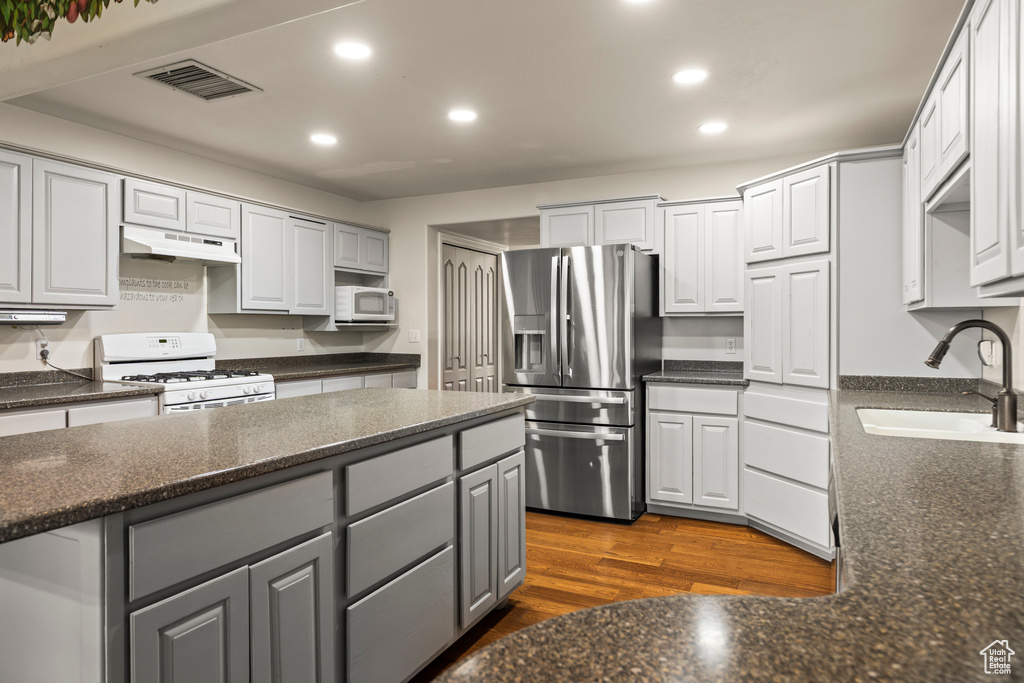 Kitchen featuring white appliances, a sink, gray cabinetry, under cabinet range hood, and recessed lighting