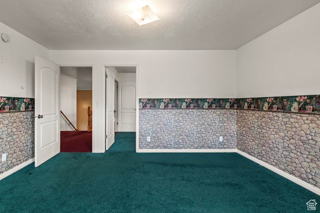 Unfurnished room with dark colored carpet, wainscoting, a smoke detector, and a textured ceiling