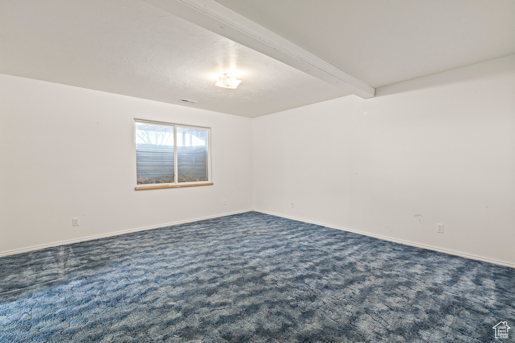 Spare room featuring dark colored carpet, baseboards, and beam ceiling
