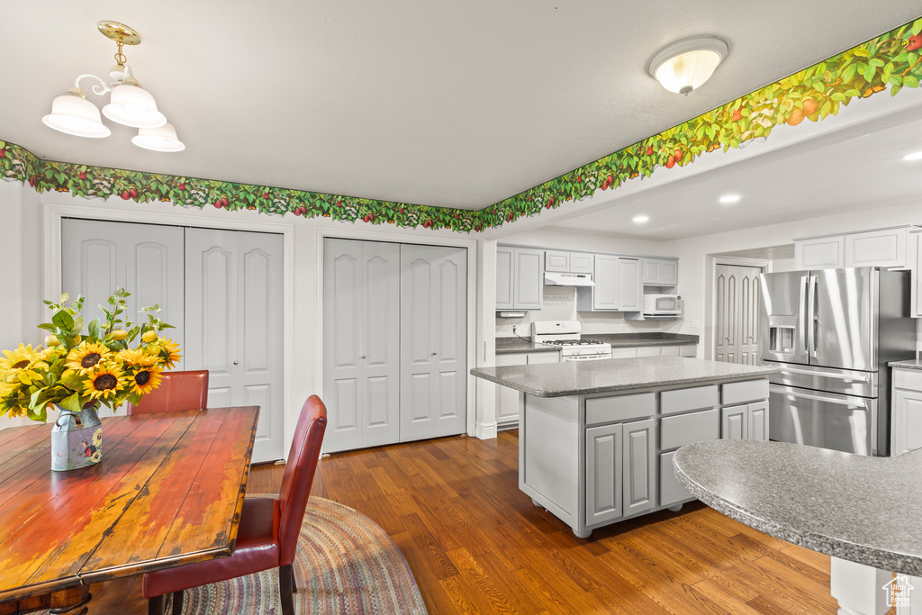 Kitchen featuring white appliances, a kitchen island, dark wood-style floors, under cabinet range hood, and white cabinetry