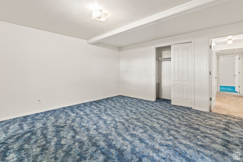 Unfurnished bedroom featuring carpet, baseboards, a textured ceiling, and a closet