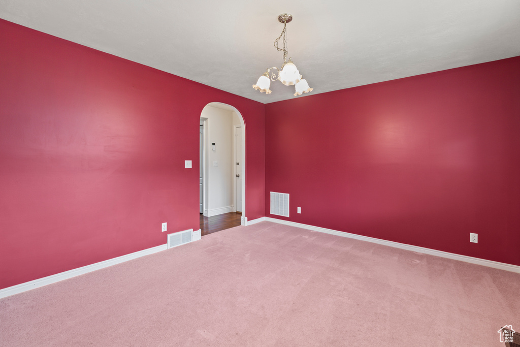 Carpeted spare room with arched walkways, a chandelier, and baseboards