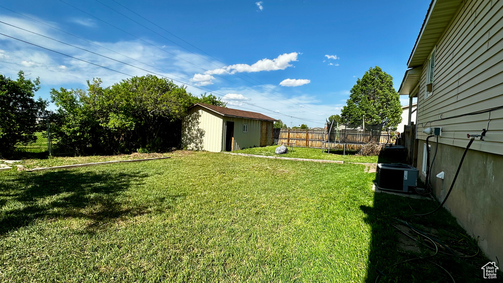 View of yard with a trampoline, a shed, an outbuilding, and central AC