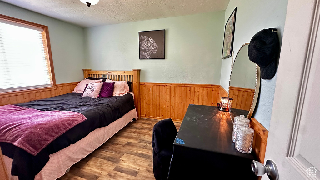 Bedroom with wood finished floors, wood walls, wainscoting, and a textured ceiling