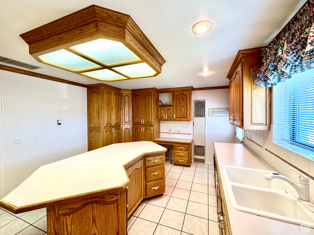 Kitchen featuring a sink, brown cabinets, light tile patterned floors, a center island, and light countertops