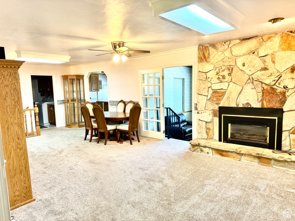 Carpeted dining area with crown molding, ceiling fan, and a fireplace