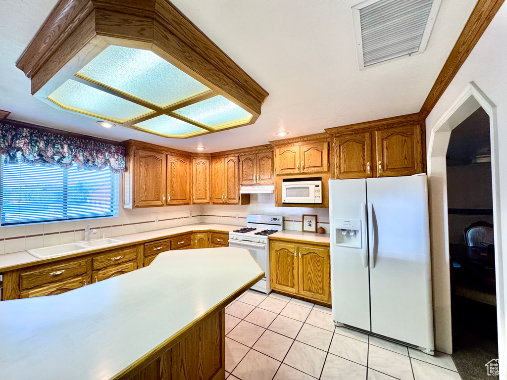 Kitchen featuring white appliances, under cabinet range hood, brown cabinetry, a sink, and recessed lighting