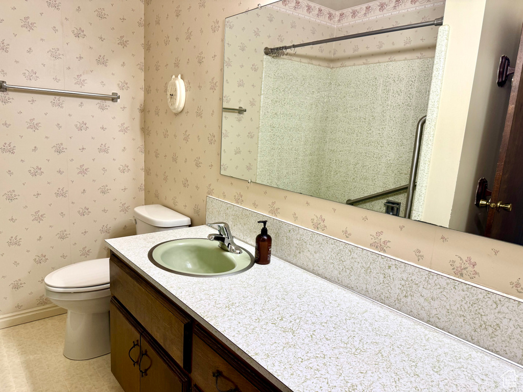 Full bathroom featuring toilet, vanity, wallpapered walls, and a shower