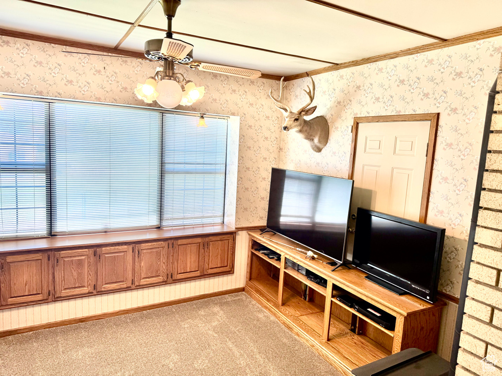 Unfurnished living room with wallpapered walls, light carpet, crown molding, a chandelier, and healthy amount of natural light