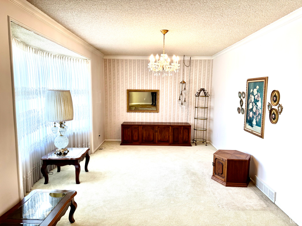 Sitting room featuring a chandelier, carpet floors, ornamental molding, a textured ceiling, and wallpapered walls