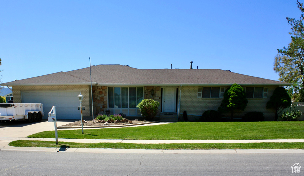 Ranch-style house featuring an attached garage, a front lawn, concrete driveway, brick siding, and stone siding