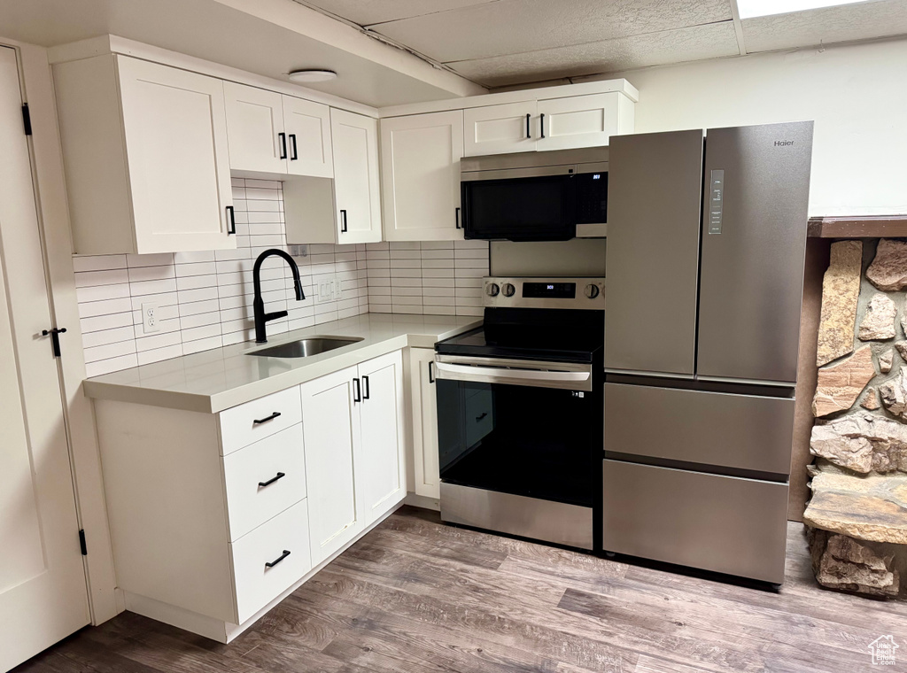 Kitchen featuring stainless steel appliances, a sink, white cabinets, light countertops, and dark wood-style flooring