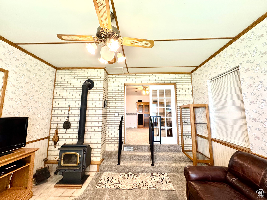 Living room with ceiling fan, wallpapered walls, crown molding, a wood stove, and a wainscoted wall