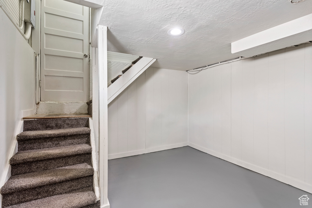 Finished below grade area featuring stairs, a textured ceiling, and recessed lighting
