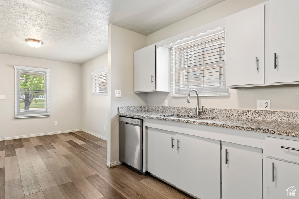 Kitchen featuring dishwasher, a sink, wood finished floors, white cabinets, and a textured ceiling