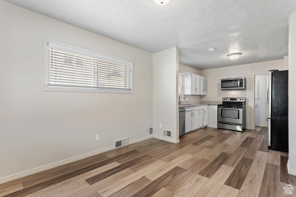 Kitchen with stainless steel appliances, light wood-style flooring, light countertops, a textured ceiling, and baseboards
