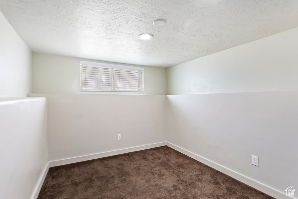 Unfurnished room featuring dark carpet, a textured ceiling, and baseboards