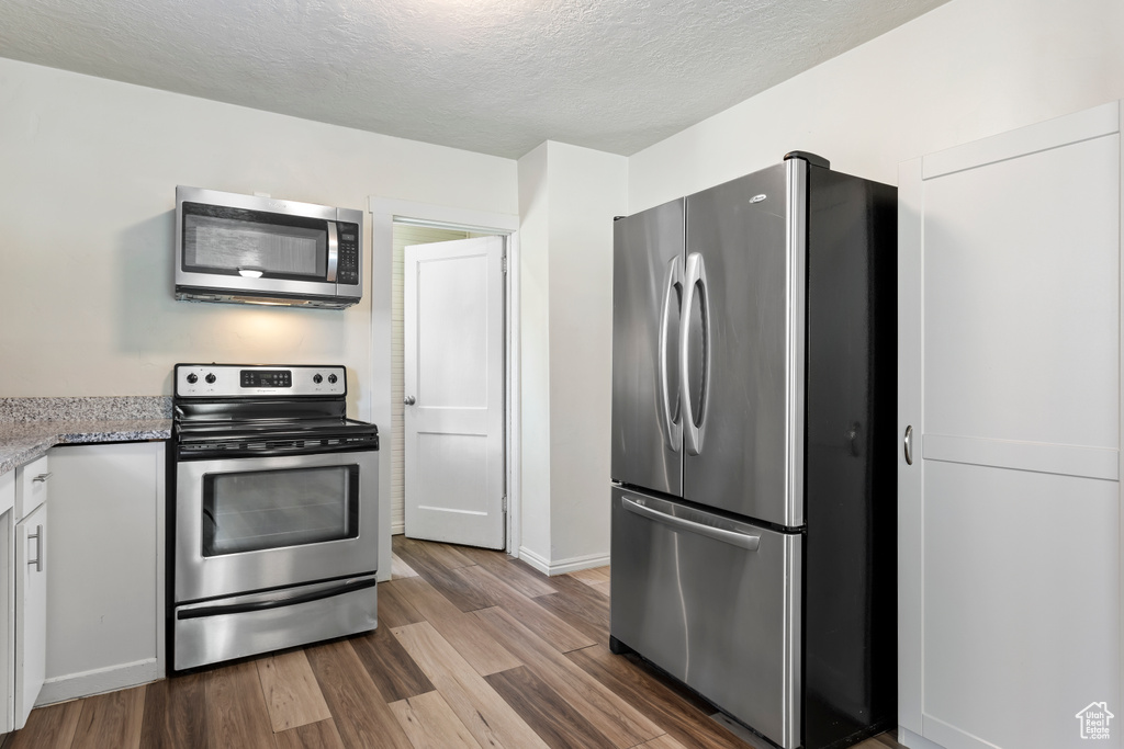 Kitchen featuring stainless steel appliances, wood finished floors, a textured ceiling, baseboards, and white cabinetry