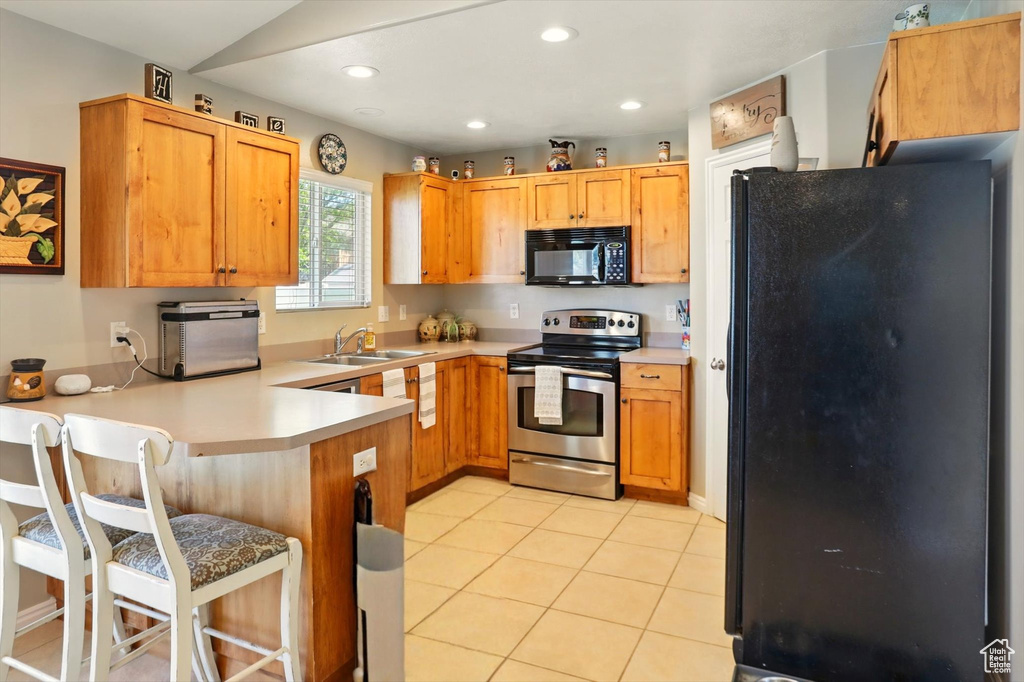 Kitchen with black appliances, a peninsula, a sink, light countertops, and recessed lighting
