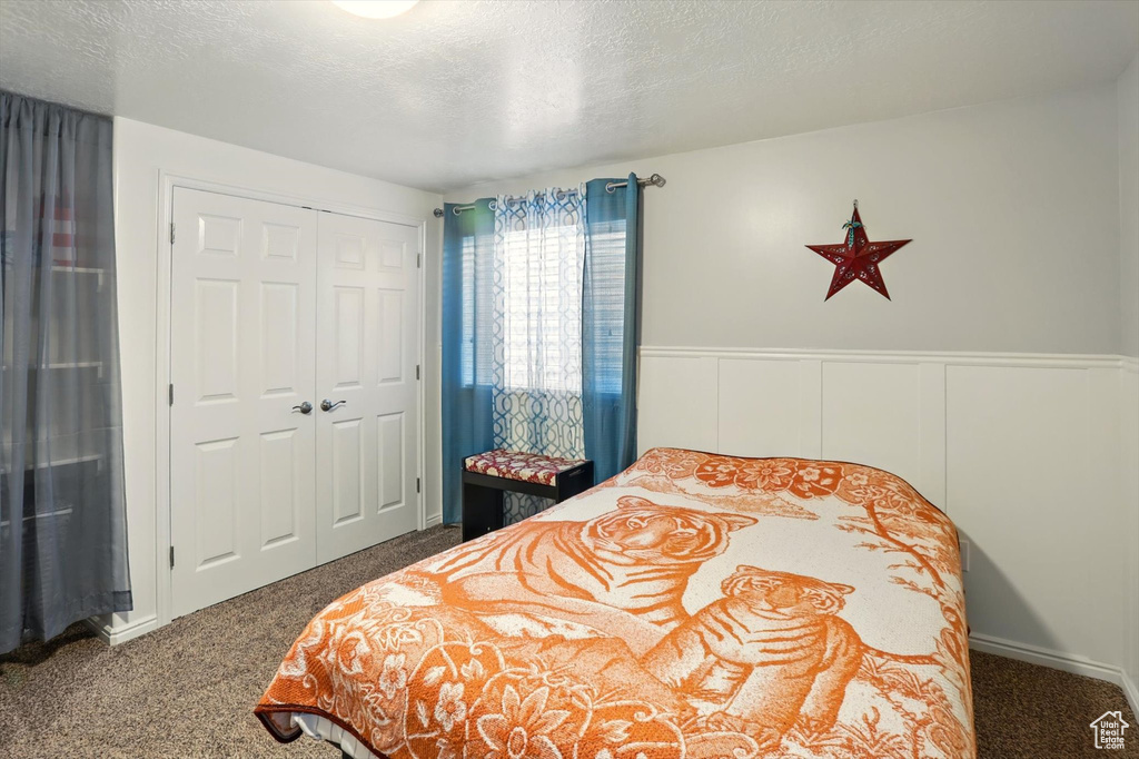 Bedroom featuring carpet floors, a closet, wainscoting, and a textured ceiling