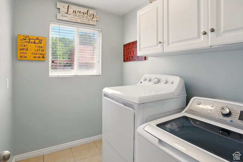 Washroom featuring cabinet space, separate washer and dryer, light tile patterned flooring, and baseboards