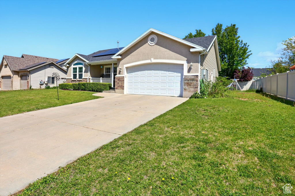 Ranch-style home with an attached garage, driveway, roof mounted solar panels, and stucco siding