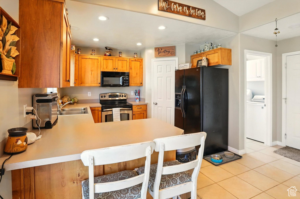 Kitchen with black appliances, a sink, washing machine and clothes dryer, a peninsula, and light countertops