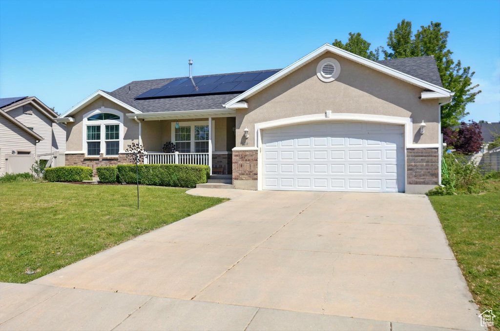 Ranch-style house featuring stucco siding, a porch, an attached garage, a front yard, and roof mounted solar panels