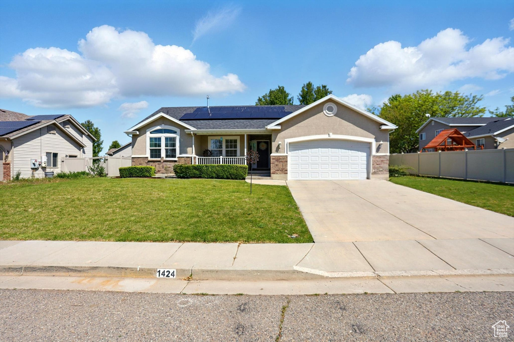 View of front of property featuring covered porch, roof mounted solar panels, an attached garage, driveway, and stucco siding