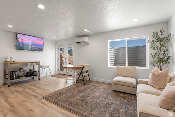 Living area with a wall mounted air conditioner, a textured ceiling, recessed lighting, wood finished floors, and baseboards