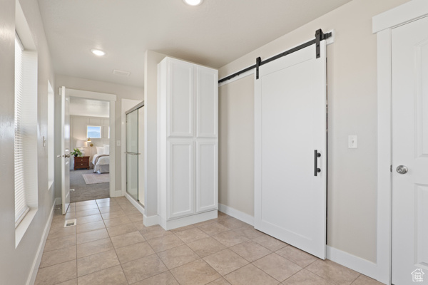 Hallway with a barn door, light tile patterned flooring, baseboards, and recessed lighting