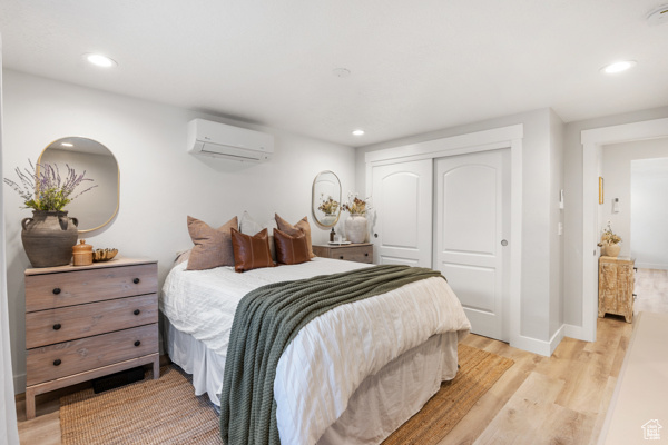 Bedroom with light wood-type flooring, a wall unit AC, a closet, recessed lighting, and baseboards