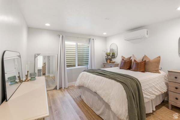 Bedroom featuring a wall mounted air conditioner, light wood-style floors, and recessed lighting