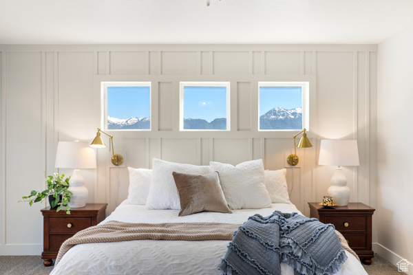 Carpeted bedroom with baseboards, a decorative wall, and multiple windows