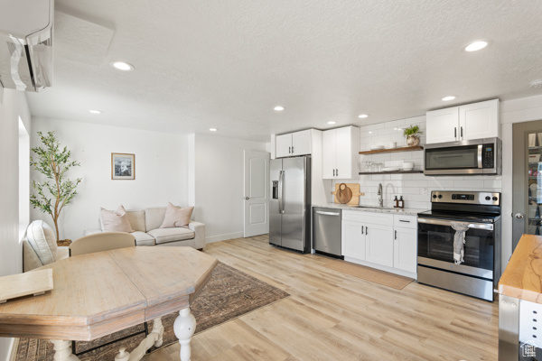 Kitchen with appliances with stainless steel finishes, a sink, decorative backsplash, light wood finished floors, and white cabinets
