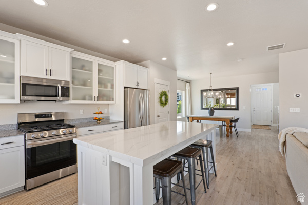Kitchen featuring appliances with stainless steel finishes, a center island, white cabinetry, a kitchen bar, and a chandelier