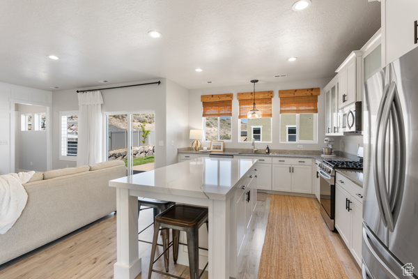 Kitchen with stainless steel appliances, recessed lighting, light wood-type flooring, a kitchen bar, and white cabinetry
