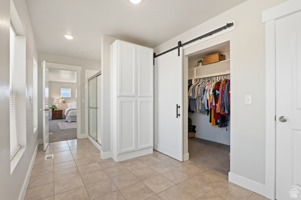 Unfurnished bedroom featuring light tile patterned flooring, light colored carpet, a spacious closet, a barn door, and baseboards