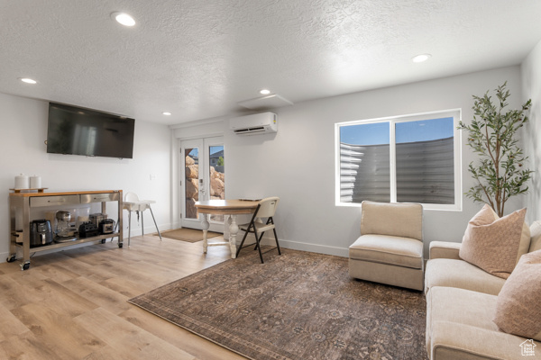 Living area with a wall mounted AC, wood finished floors, a textured ceiling, recessed lighting, and baseboards