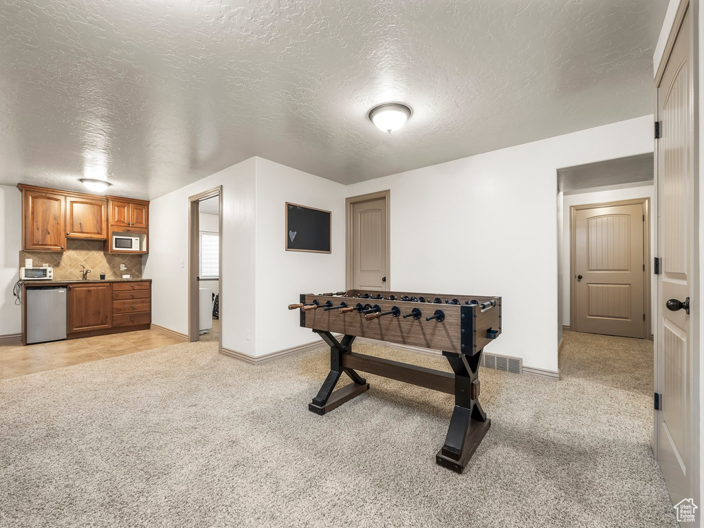 Rec room with light carpet, a textured ceiling, a sink, and baseboards