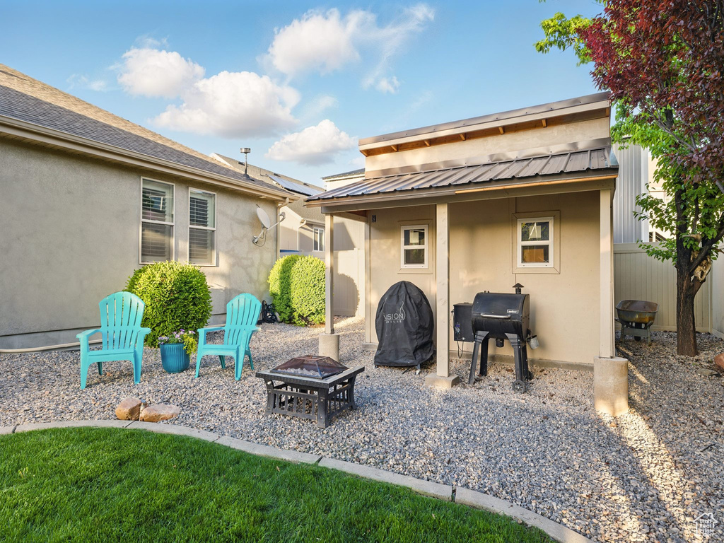 Rear view of house featuring a fire pit, stucco siding, metal roof, and fence