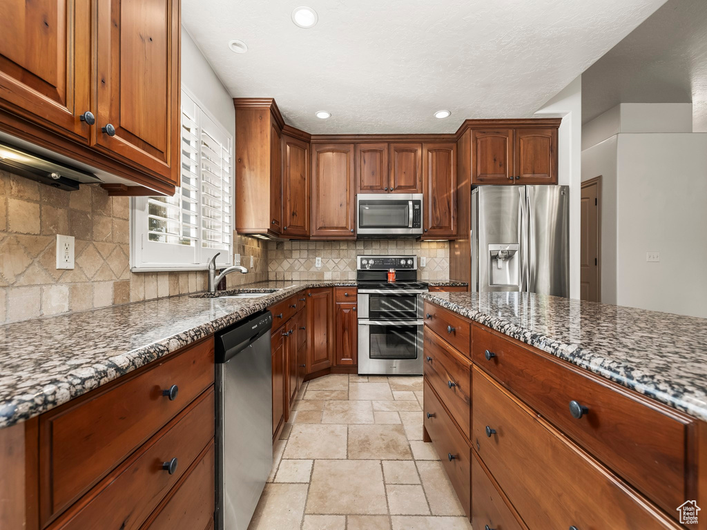 Kitchen with appliances with stainless steel finishes, a sink, stone tile floors, dark stone counters, and recessed lighting