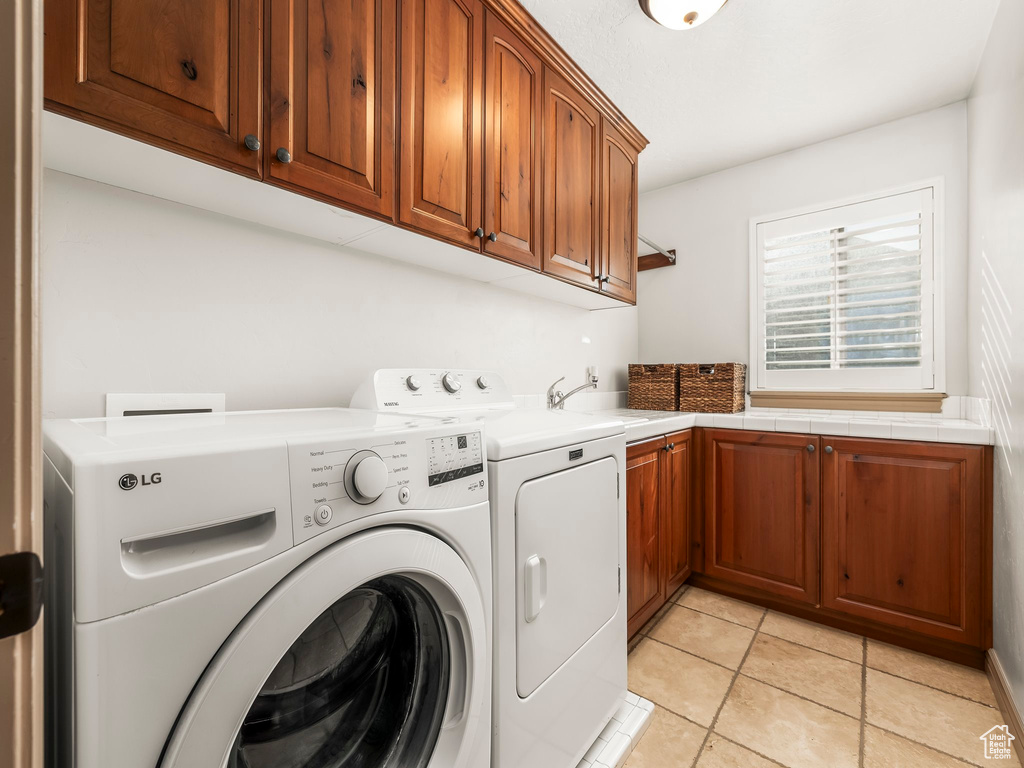 Laundry room featuring washing machine and clothes dryer, cabinet space, and light tile patterned floors