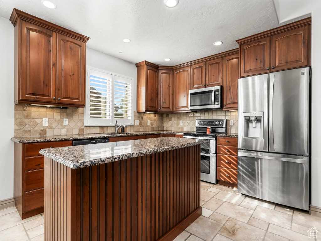 Kitchen with stainless steel appliances, dark stone counters, recessed lighting, backsplash, and a center island