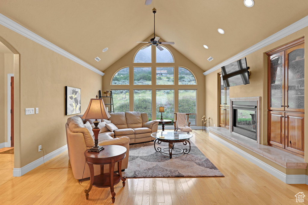 Living room with light wood-style floors, a glass covered fireplace, a ceiling fan, arched walkways, and baseboards