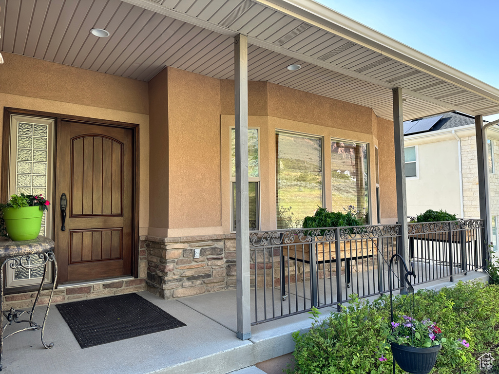 View of exterior entry featuring stucco siding, covered porch, and stone siding