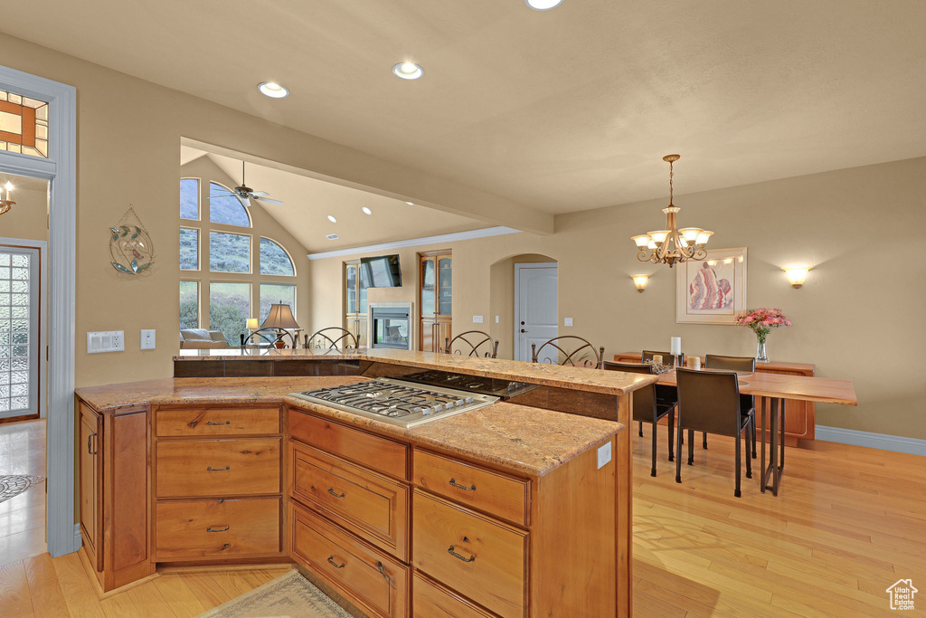 Kitchen featuring stainless steel gas stovetop, arched walkways, light stone countertops, light wood-type flooring, and recessed lighting