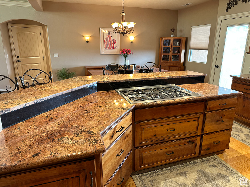 Kitchen with stainless steel gas cooktop, light wood-style flooring, brown cabinetry, and a chandelier