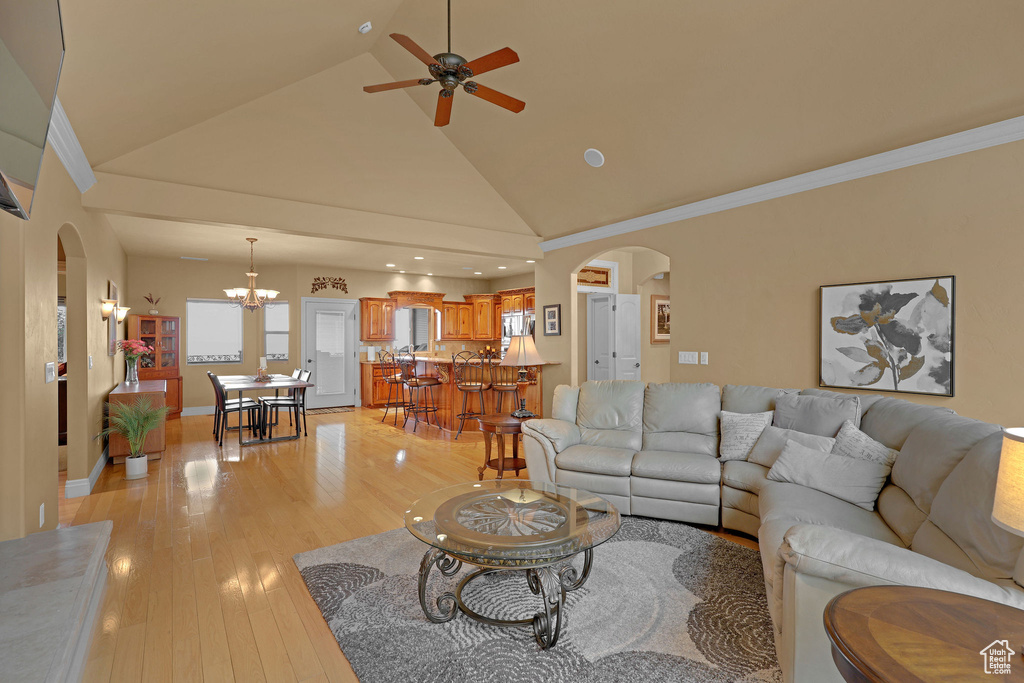 Living area with arched walkways, a chandelier, light wood-style flooring, high vaulted ceiling, and a ceiling fan